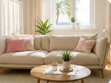 Bright, tidy living room with a beige sofa, pink cushions and a palm tree outside the window